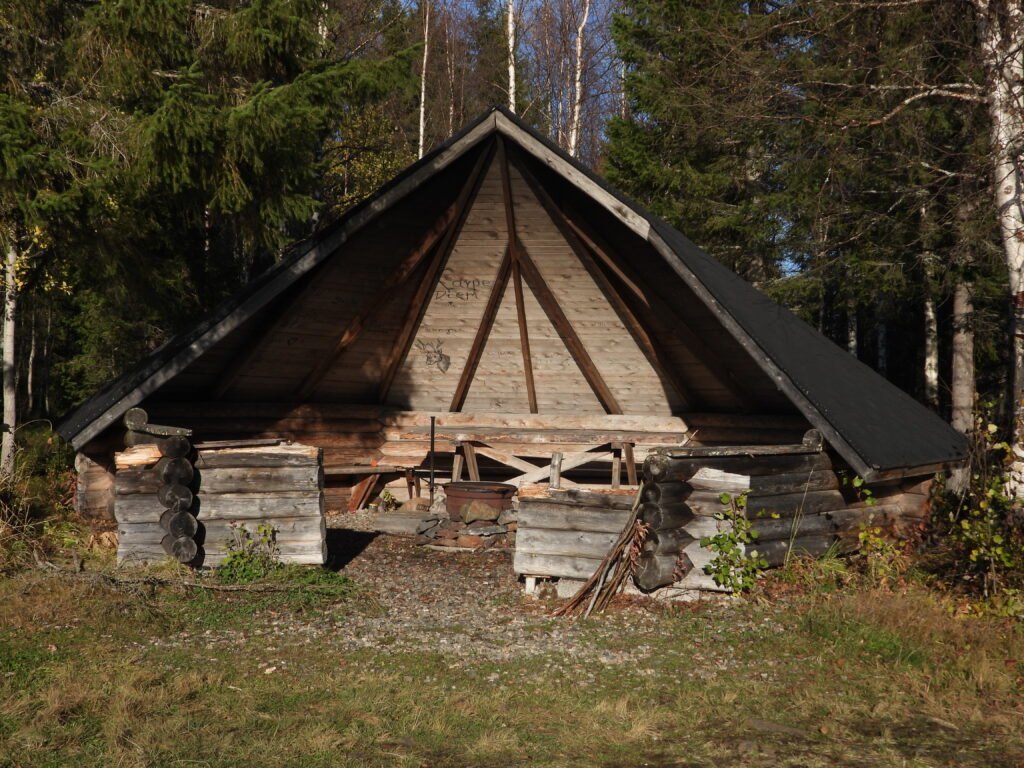 Cabane en bois dans une forêt en Finlande, avec un toit en pente et des éléments en bois visibles.