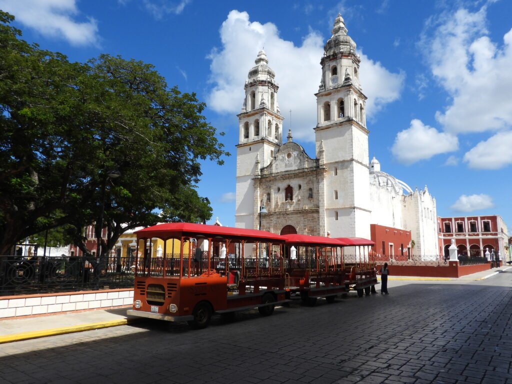 Église avec deux tours et tramway rouge à Mérida, Mexique, sous un ciel bleu avec quelques nuages.