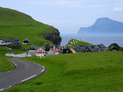 Village coloré à Gjógv, îles Féroé, avec des maisons aux toits noirs et rouges, surplombant la mer et les falaises verdoyantes.
