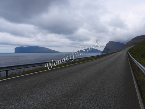 Route longeant la mer avec des îles en arrière-plan à Fuglafjørður, Îles Féroé, sous un ciel nuageux.