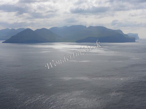 Îles Féroé, Trollanes, avec des montagnes se reflétant sur une mer calme sous un ciel nuageux.