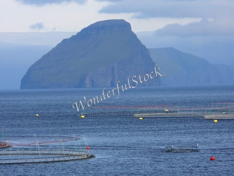 Montagne de Slættaratindur à Gasadalur, Îles Féroé, avec des installations aquacoles et un bateau sur l'eau.