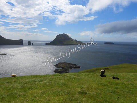 Paysage côtier à Gasadalur, Îles Féroé, avec des collines verdoyantes et des formations rocheuses émergeant de la mer.
