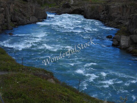 Une rivière aux eaux vives coule entre des rochers, entourée de verdure, en Islande.