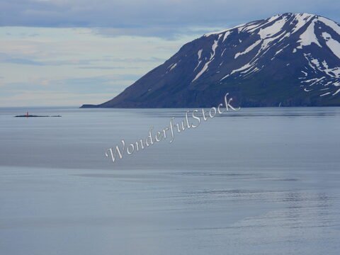 Montagne avec neige et mer calme en Islande. Un phare orange est visible sur une petite île.