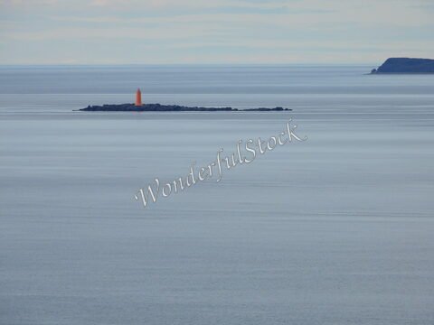 Phare orange sur une île rocheuse en Islande, entouré d'une mer calme et d'horizons lointains.