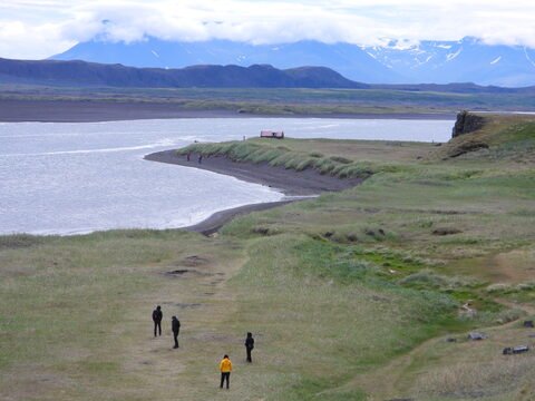 Plage de sable et prairies avec des personnes à Islande. Montagnes en arrière-plan sous un ciel nuageux.