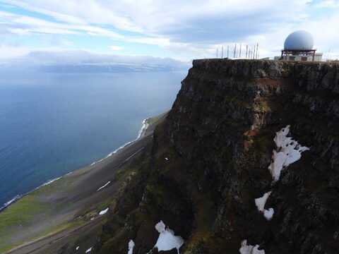 Un sommet rocheux avec une structure en forme de dôme, surplombant la mer, à Bolafjall, Islande.
