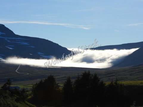 Vallée brumeuse avec des montagnes en arrière-plan à Bolungarvik, Islande. Des nuages bas se déplacent au-dessus du paysage verdoyant.