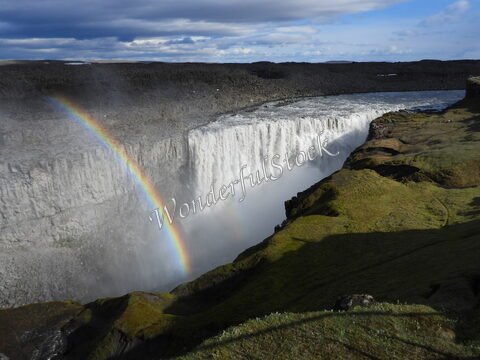 Cascade de Dettifoss en Islande, avec un arc-en-ciel au-dessus et des formations rocheuses environnantes.