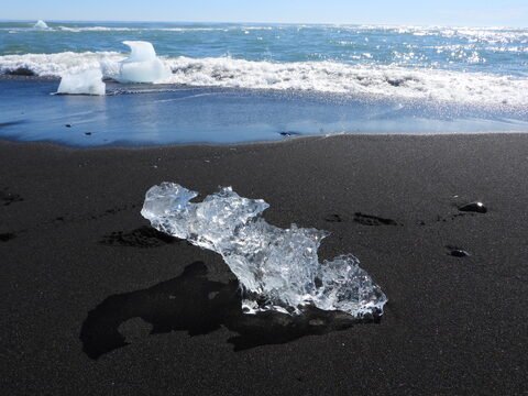 Glace sur la plage de sable noir à Diamond Beach, Islande, avec des vagues en arrière-plan.