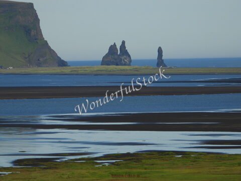 Trois formations rocheuses se dressent au large de Dyrhólaey, en Islande, entourées d'eaux calmes et de rives noires.