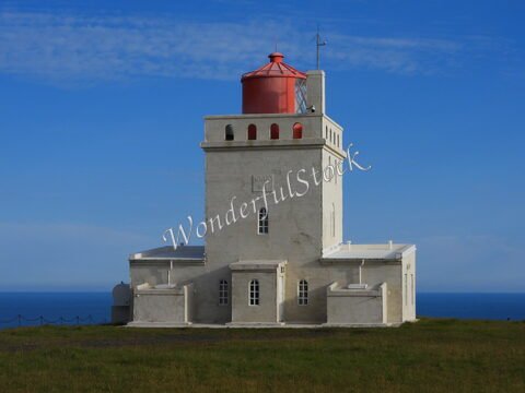 Phare blanc avec un dôme rouge à Dyrhólaey, Islande, surplombant l'océan.