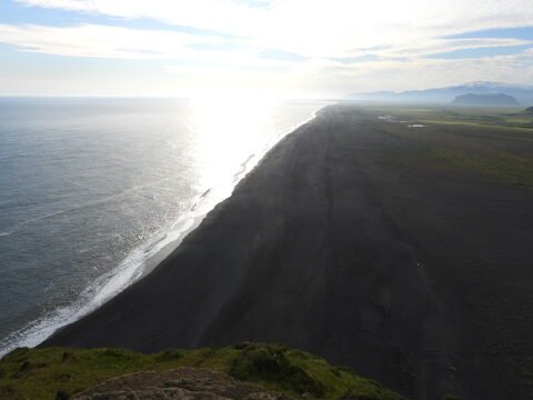Plage de sable noir à Dyrhólaey, Islande, avec l'océan et des montagnes en arrière-plan.
