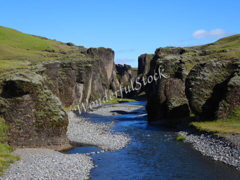 Gorges de Fjaðrárgljúfur en Islande, avec une rivière serpentant entre des parois rocheuses et une végétation verdoyante.