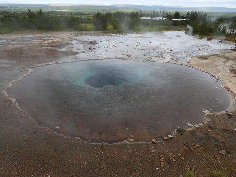 Geysir en Islande, avec un trou d'eau chaude entouré de vapeur et de terrain rocheux.