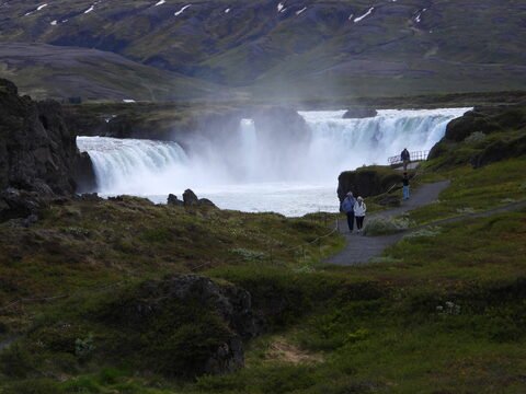 Chutes d'eau à Goðafoss, Islande, avec des visiteurs sur un sentier bordé de verdure.