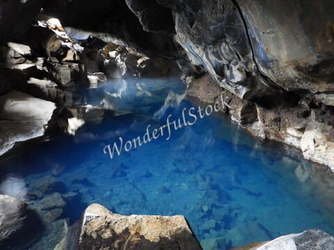 Une source géothermique avec une eau bleue, entourée de roches, à Grjótagjá, Islande.