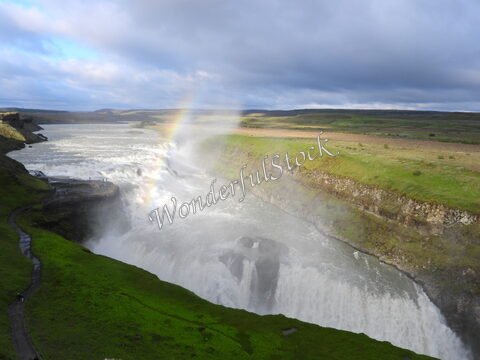Gullfoss en Islande, une chute d'eau impressionnante entourée de verdure et de formations rocheuses, sous un ciel nuageux.