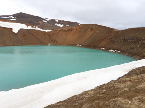 Lac turquoise entouré de collines arides et de neige à Krafla, Islande.