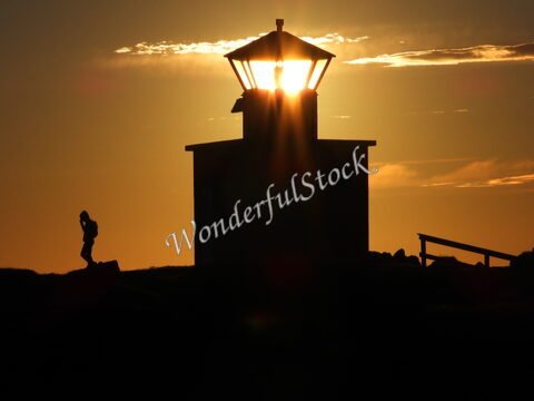 Un phare silhouetté au coucher de soleil à Öndverðarnes, Islande, avec une personne marchant à proximité.