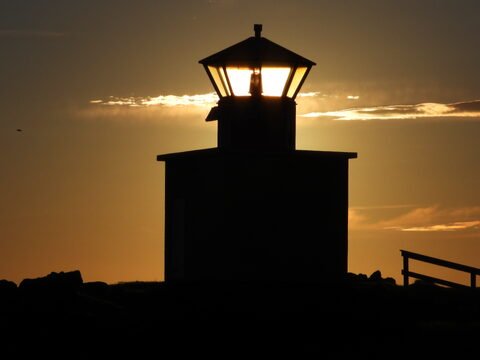 Phare silhouette au coucher de soleil à Öndverðarnes, Islande, avec des nuages et des rochers en arrière-plan.
