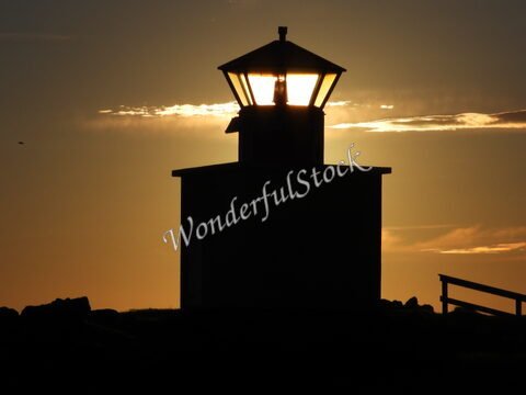 Phare silhouette au coucher de soleil à Öndverðarnes, Islande, avec des nuages et des rochers en arrière-plan.