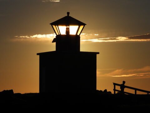 Phare silhouetté au coucher du soleil à Öndverðarnes, Islande, avec un homme près d'une barrière.