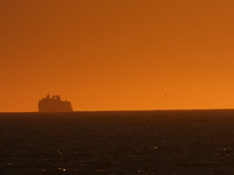 Un navire silhouette se profile sur l'horizon marin à Öndverðarnes, Islande, sous un ciel orange.