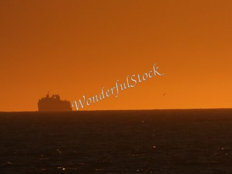 Un navire silhouette se profile sur l'horizon marin à Öndverðarnes, Islande, sous un ciel orange.