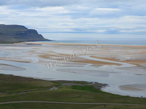 Plage de Rauðisandur en Islande, avec des formations de sable et d'eau, entourée de collines et d'un ciel nuageux.