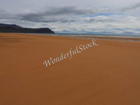 Plage de sable orange à Rauðisandur, Islande, avec des collines en arrière-plan et un ciel nuageux.