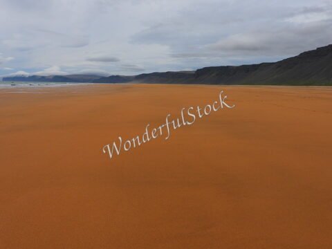 Plage de sable orange à Rauðisandur, Islande, avec des montagnes en arrière-plan et un ciel nuageux.