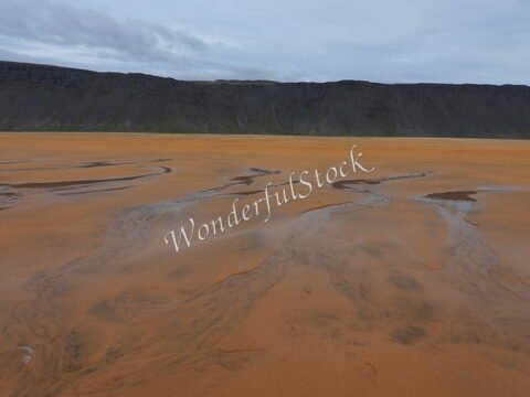 Sable orange et formations de cours d'eau sur la plage de Rauðisandur, Islande. Montagnes sombres en arrière-plan.
