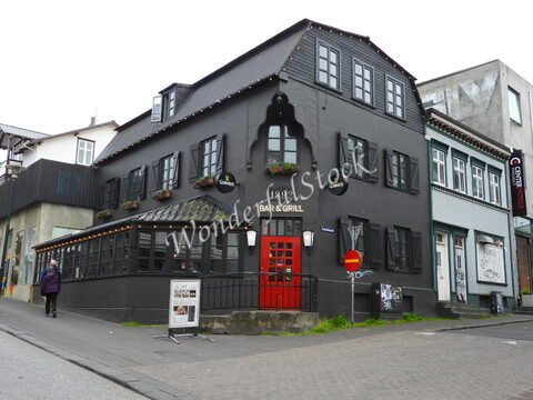 Bâtiment noir avec des volets, une porte rouge et des panneaux de restaurant, situé à Reykjavík, Islande.