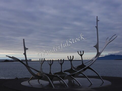 Sculpture moderne à Reykjavík, Islande, représentant un drakkar, surplombant la mer et le ciel nuageux.