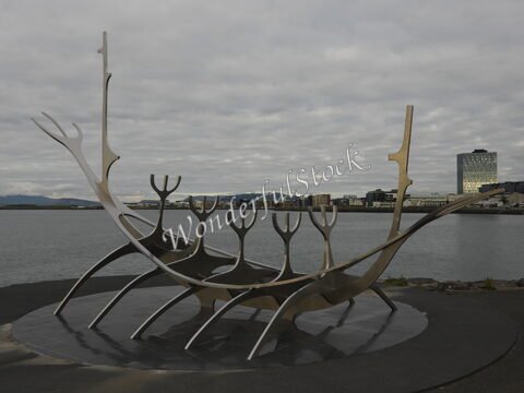 Sculpture en métal représentant un drakkar à Reykjavík, Islande, avec des bâtiments modernes en arrière-plan et une mer calme.