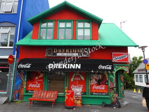 Bâtiment coloré avec toit vert et enseigne "Drekinn" à Reykjavík, Islande, avec des affiches de boissons et un banc en bois devant.