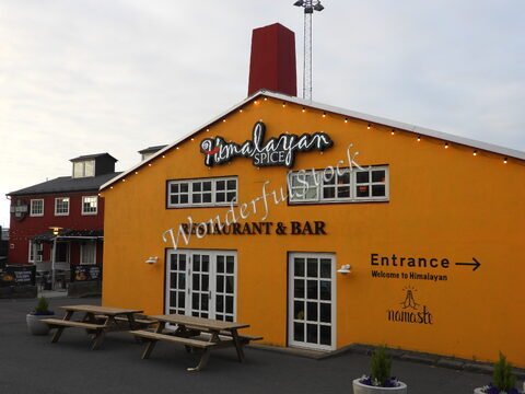 Restaurant coloré "Himalayan Spice" à Reykjavík, Islande, avec des tables en bois et une façade jaune.
