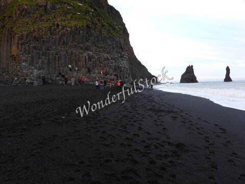Plage de sable noir à Reynisfjara, Islande, avec des colonnes de basalte et des formations rocheuses en arrière-plan.