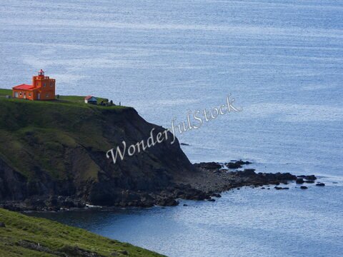 Phare orange sur une falaise surplombant la mer à Sauðanesviti, Islande, avec quelques bâtiments et rochers au bord de l'eau.
