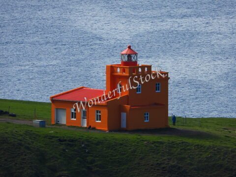 Phare orange à Sauðanesviti, Islande, face à la mer, avec une personne à proximité sur une pelouse verte.