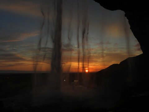Cascades de Seljalandsfoss en Islande, avec un coucher de soleil et des silhouettes de rochers en arrière-plan.