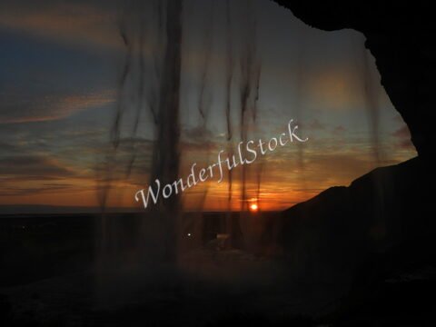 Cascades de Seljalandsfoss en Islande, avec un coucher de soleil et des silhouettes de rochers en arrière-plan.