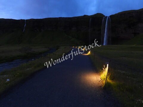 Cascade Seljalandsfoss en Islande, éclairage le long d'un chemin, avec des falaises verdoyantes en arrière-plan.