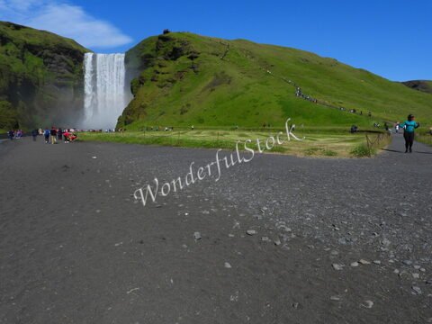 Skógafoss en Islande, avec des visiteurs admirant la chute d'eau et la végétation verdoyante environnante.