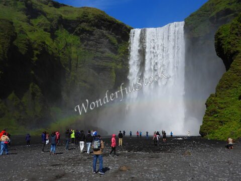 Chute d'eau à Skógafoss, Islande, avec des visiteurs admirant le paysage verdoyant et le brouillard créé par la cascade.