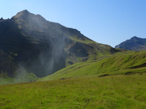 Champs verdoyants avec des montagnes en arrière-plan, Skógafoss, Islande.