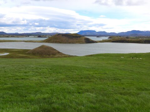 Lacs et collines verdoyantes à Skútustaðagígar, Islande, avec des montagnes en arrière-plan sous un ciel nuageux.
