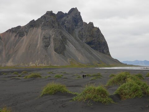 Vaste étendue de sable noir avec des herbes, dominée par la montagne Vesturhorn, en Islande.
